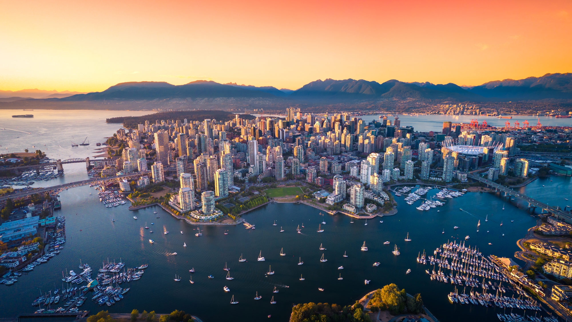 An aerial shot of downtown Vancouver, showing mountains in the background and the ocean.