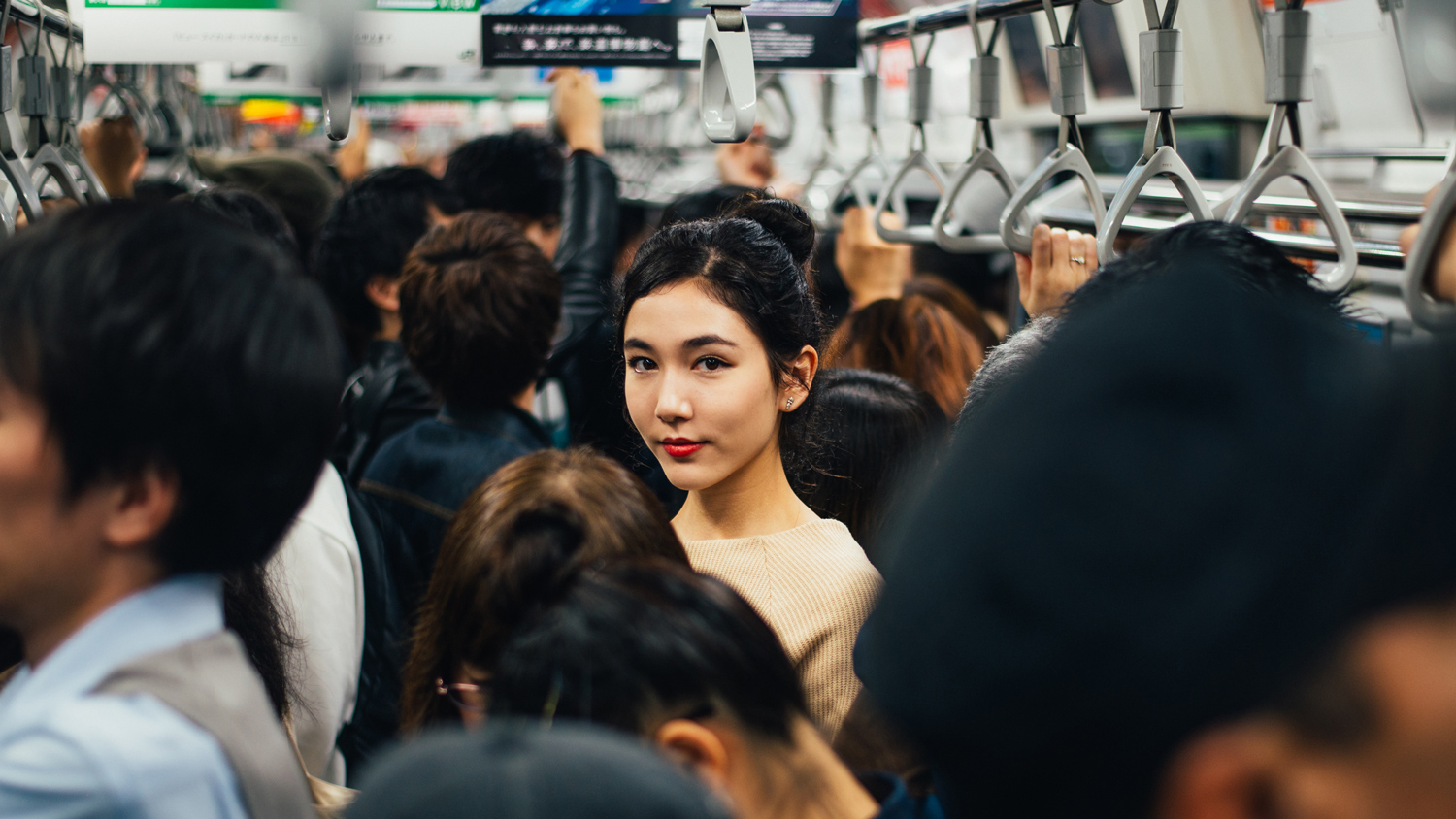 A woman standing on a crowded train looking directly at the camera.